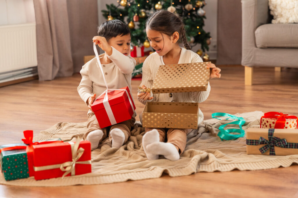 christmas, winter holidays and childhood concept - happy little girl and boy opening gifts sitting on floor at home